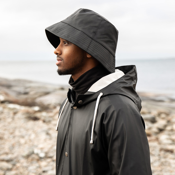 Man på en strand i svart regnjacka och svart regnhatt